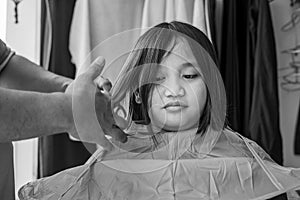 Asian young girl is getting haircut at home from the father. Young teenage girl. Monochrome, black and white