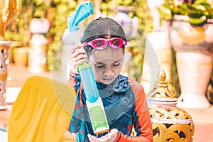 Young girl kid is playing with water gun in a tropical resort in Thailand