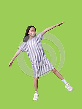 Asian young girl kid standing on one leg for balance and arms outstretched or keeping arms raised isolated on green background.