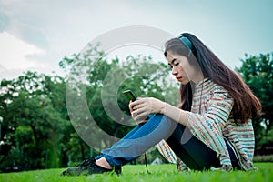 Asian young girl listening to music from a smartphone using headphones. At public park the city center happy and relax On his