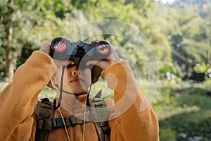 Asian young girl looking through a binoculars searching for an imagination or exploration in summer day in the forest