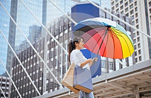 Asian young girl smling and holding shopping bags with umbrella in city