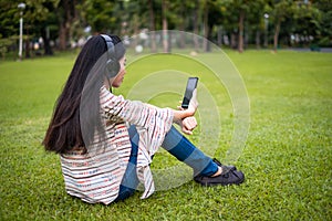 Asian young girl stands listening to music from a smartphone using headphones and copy space. At public park the city center happy