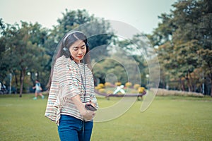 Asian young girl stands listening to music from a smartphone using headphones and copy space. At public park the city center happy