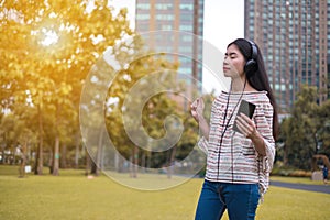 Asian young girl stands listening to music from a smartphone using headphones. At public park the city center happy and relax On