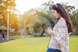 Asian young girl stands listening to music from a smartphone using headphones. At public park the city center happy and relax On