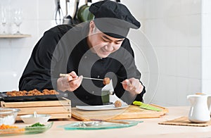 Asian young handsome chef man, in black uniform, smiling while cooking japanese food called takoyaki in hot pan with ingredients