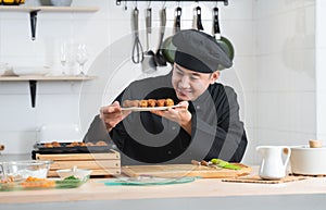 Asian young handsome chef man, in black uniform, smiling while looking at japanese food called takoyaki in plate at kitchen