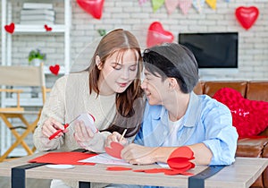 Asian young handsome male boyfriend sitting on sofa smiling cuddling with beautiful female girlfriend holding red heart shape