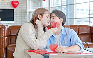 Asian young handsome male boyfriend sitting on sofa smiling cuddling with beautiful female girlfriend holding red heart shape