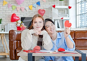 Asian young handsome male boyfriend sitting on sofa smiling cuddling with beautiful female girlfriend holding red heart shape