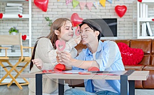 Asian young handsome male boyfriend sitting on sofa smiling cuddling with beautiful female girlfriend holding red heart shape