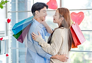 Asian young handsome male boyfriend standing smiling hugging cuddling with beautiful female girlfriend holding paper shopping bags