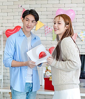 Asian young handsome male boyfriend standing smiling playing cuddling with beautiful female girlfriend holding red heart shape