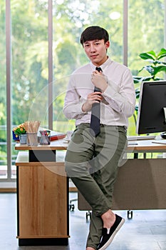 Asian young handsome professional successful male businessman employee in formal business shirt adjusting necktie sitting leaning
