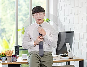 Asian young handsome professional successful male businessman employee in formal business shirt adjusting necktie sitting leaning