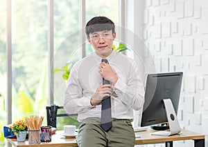 Asian young handsome professional successful male businessman employee in formal business shirt adjusting necktie sitting leaning