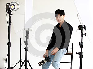 Asian young handsome successful happy male model photographer wears black long sleeve shirt and blue jeans hold DSLR camera in