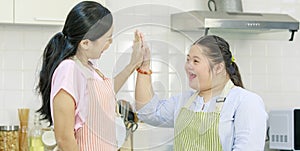 Asian young happy chubby down syndrome autistic daughter in apron and lovely mother standing smiling laughing in kitchen showing