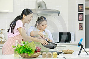 Asian young happy chubby down syndrome autistic daughter in apron and lovely mother standing smiling laughing in kitchen showing