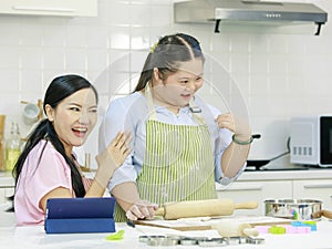 Asian young happy chubby down syndrome autistic daughter wears apron standing smiling laughing in kitchen touching hands with