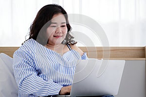 Asian young happy fat chubby woman lay down have fun laughing happily lean on white pillow on bed using laptop computer to watch