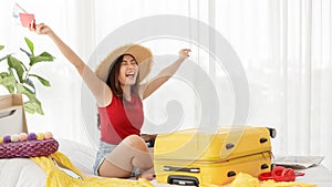 Asian young happy female traveler sitting on bed holding passport with air tickets with happy and excited actions while packing