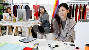 Asian young happy pretty successful female stylish fashion designer sit smiling look at camera at work desk in studio workshop