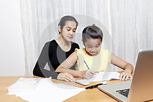 Asian young little girl using pencil to do homework with her mother. Student kid writing  homework book. Girl use computer to