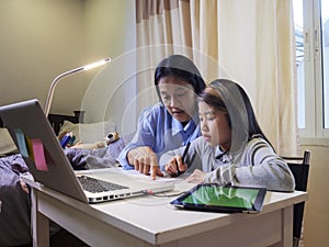 Asian young little girl using pencil to do homework with her mother. Student kid writing  homework book. Girl use computer to