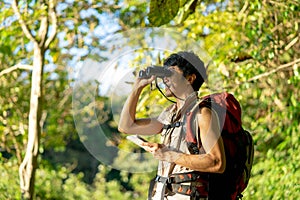 Asian young man with binoculars hiking in forest. Summer vacation