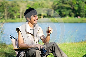 Asian young man freelancer sitting on chair and relaxing at camping site in forest or meadow. Outdoor activity in summer. leisure