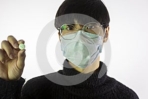 Asian young man in glasses, protective mask against covid-19 with pill in hand