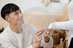 Asian young man kneeling and proposing to his girlfriend with ring