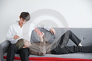 Asian young man lying on his boyfriend lap and using tablet on sofa at home