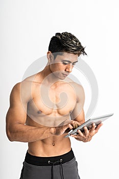 Asian young man with muscular body holding a tablet with two hand typing stand facing forward and look at a tablet