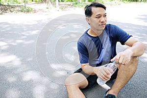 Asian young man in navy blue sportwear Thirsty and drinking water in bottle after exercise and running in garden