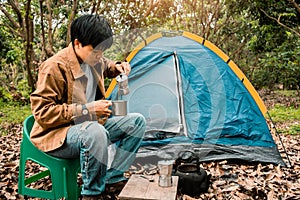 Asian young man pouring coffee maker out the tent. drinking coffee in forest, alone lifestyle vacation camping