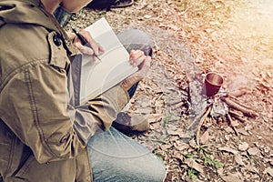 Asian young man sitting is holding a pen writing note of letter memorize memories on book in outside the tent. Loneliness camping photo