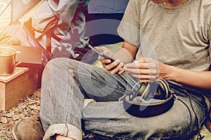 Asian young man sitting and using mobile phone in  outside the tent. Alone camping in forest