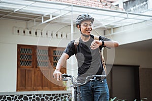 Asian young man standing with folding bike while looking her watch