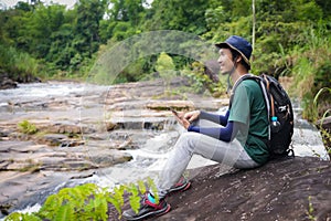 Asian young man, tall and slender, Wear your favorite blue hat, Sitting chilling on a large rock, enjoying the cool breeze, He