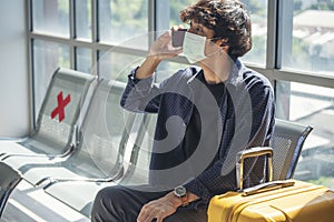 Asian young man traveller new normal holding smartphone in Airplane lounge wear face mask sitting Social distancing. New normal