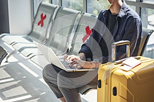 Asian young man traveller new normal using laptop computer wear face mask sitting Social distancing in Airplane lounge. New normal