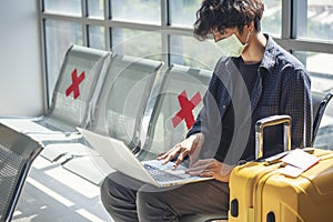 Asian young man traveller new normal using laptop computer wear face mask sitting Social distancing in Airplane lounge. New normal