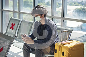 Asian young man traveller new normal wearing face mask sitting Social distancing holding smartphone in Airplane lounge. New normal