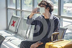 Asian young man traveller new normal wearing face mask sitting Social distancing holding smartphone in Airplane lounge. New normal