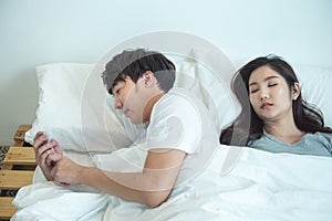 Asian young man use smart mobile phone chatting secrecy on bed while his girlfriend sleeping.Cheating boyfriend Secretly use