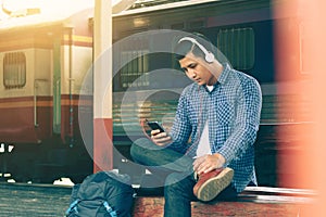 Asian young man using smartphone and listen music waiting train