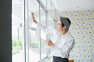 Asian young man white shirt wipe cleaning window glass with spray alcohol for sterilize in restaurant.